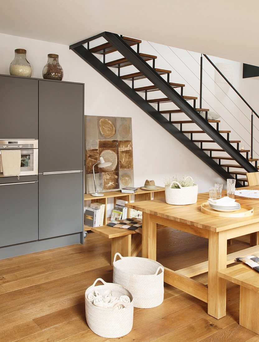Essbereich mit massiven Holzmöbeln in offener Küche neben Stahltreppe