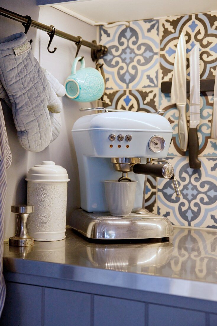 Hellblaue Retro-Espressomaschine vor Ornamentfliesen mit floralem Motiv in Landhausküche