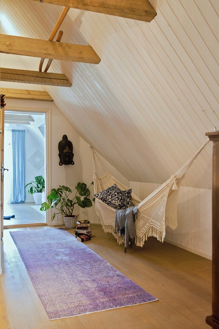 Hammock, houseplant and ethnic mask in high-ceilinged attic room