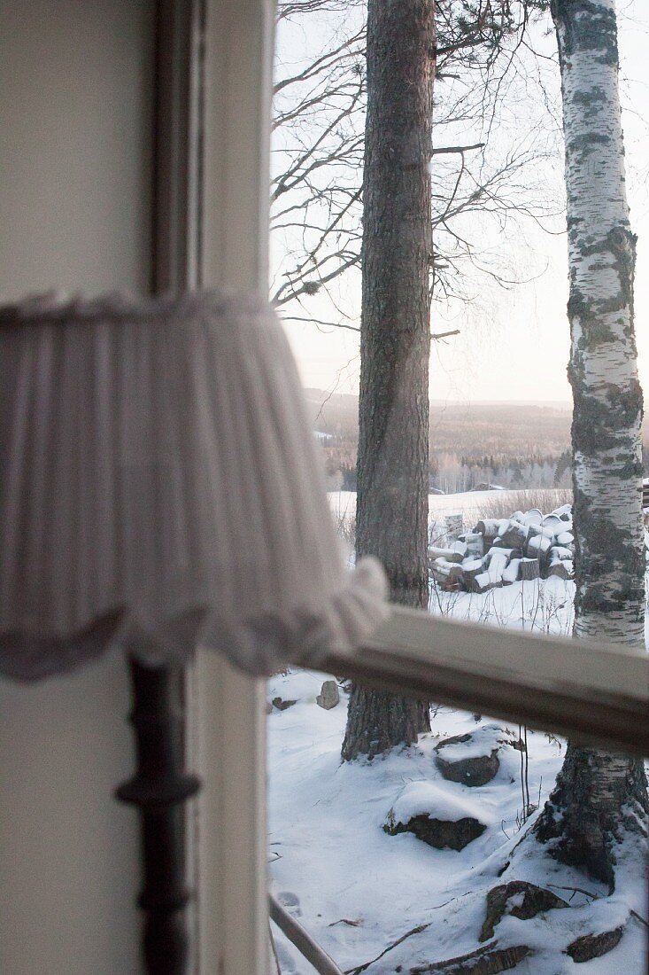 Lampe am Fenster, Blick auf verschneite Landschaft mit Bäumen