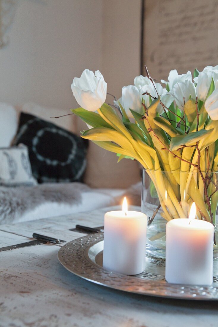 Zwei brennende Kerzen auf einem Tablett mit einem Strauß Tulpen