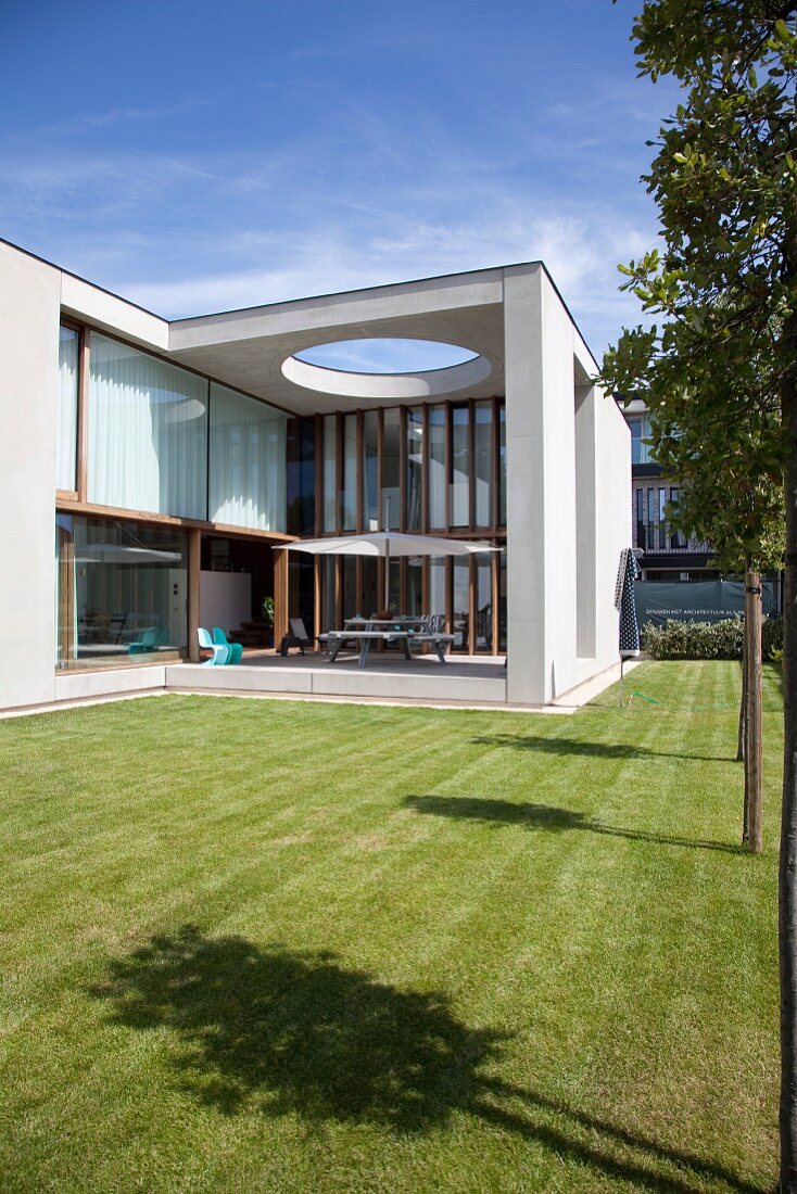 Modern architect-designed house with flat roof, glass façade, roofed terrace and manicured lawn