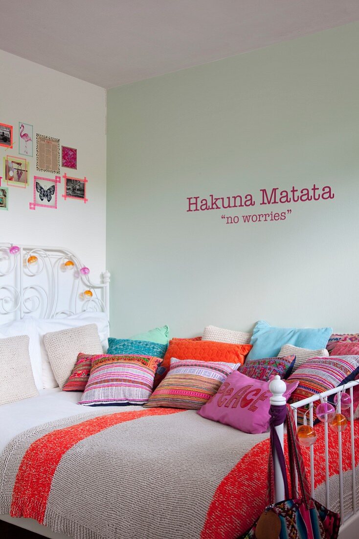Wall tattoo above bed covered with many colourful scatter cushions