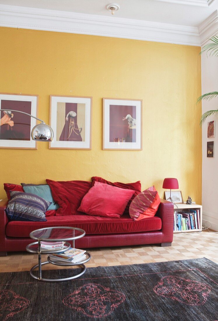 Rotes Sofa mit Kissen an gelber Wand mit Bildern und Beistelltisch auf Teppich in Altbauwohnung