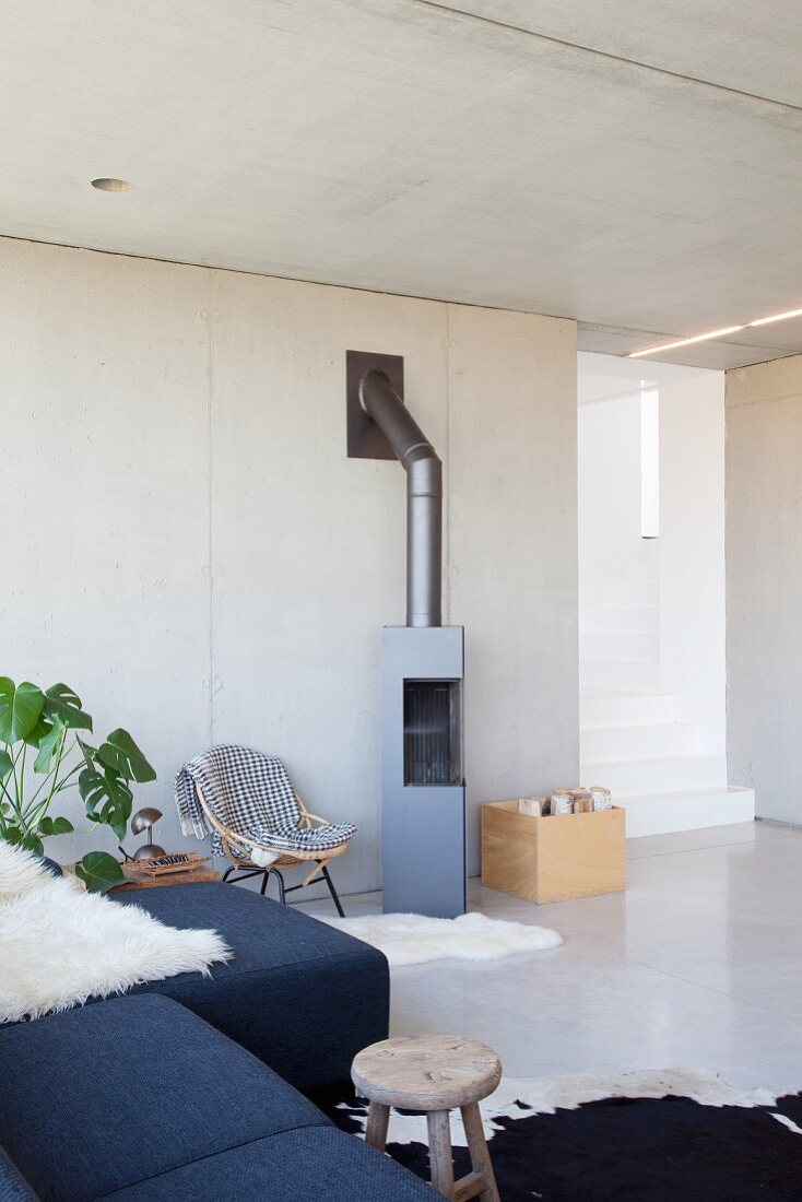 Couch, house plants and wood-burning stove in open-plan interior with concrete wall