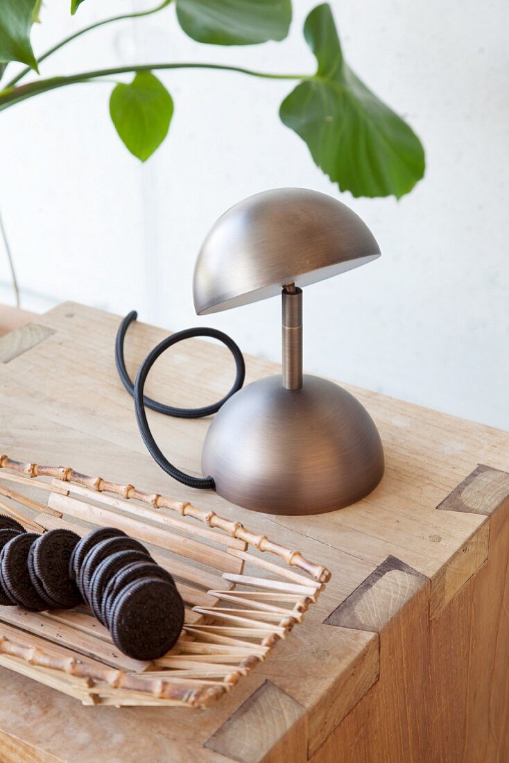Holzschale mit Keksen und Metall-Tischlampe auf Holzwürfel