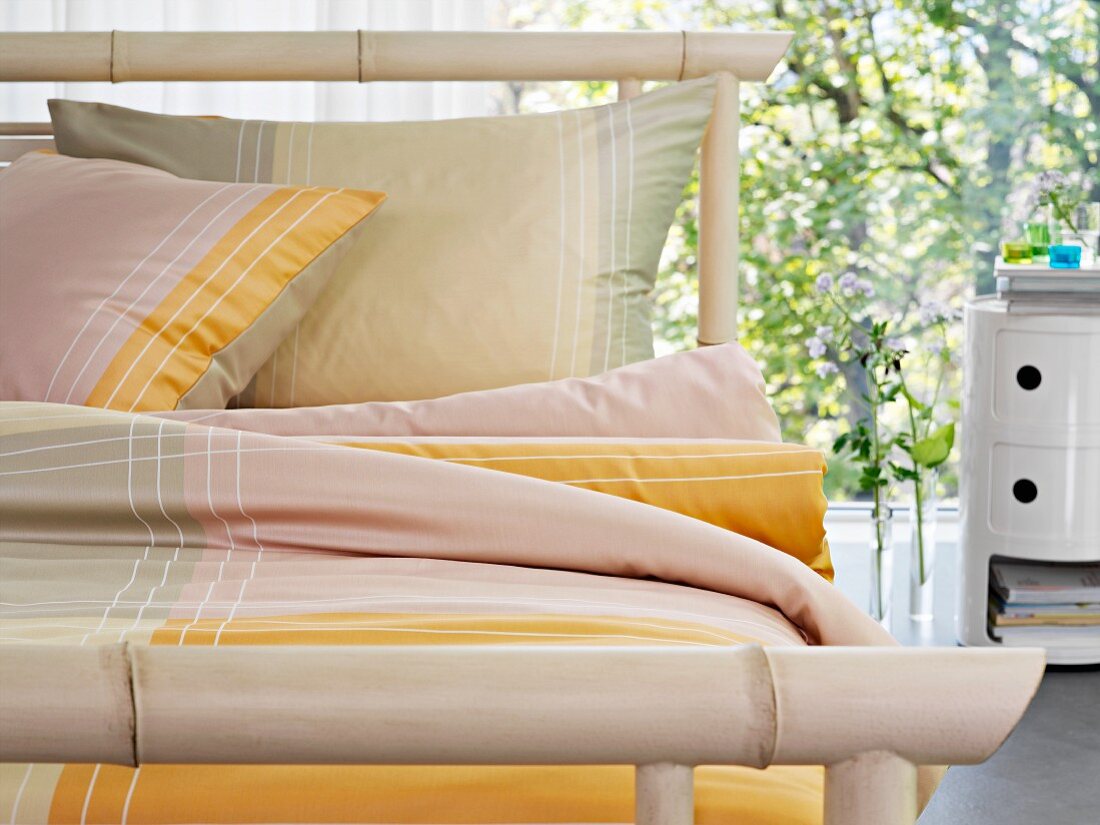 Bambus-Bett mit gelber Bettwäsche vor Fensterfront