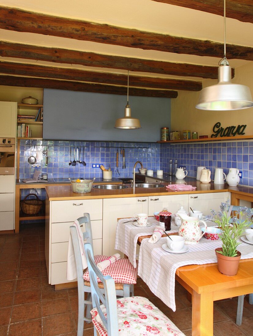 Landhausküche mit blauen Wandfliesen und Holzbalkendecke, gedeckter Esstisch mit Tischläufer