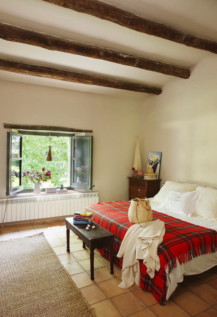 Red tartan blanket on bed, antique bedroom bench and open window