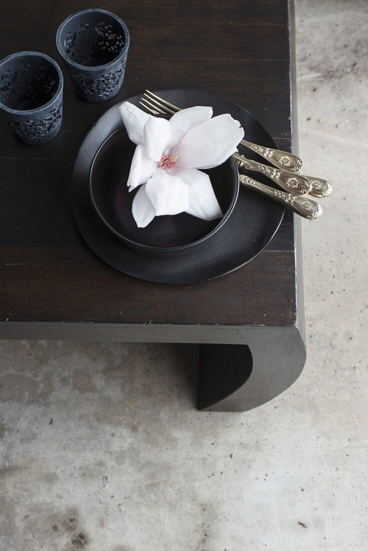 weiße Magnolienblüten in schwarzer Schale, Silberbesteck und schwarze Windlichthalter auf Tisch