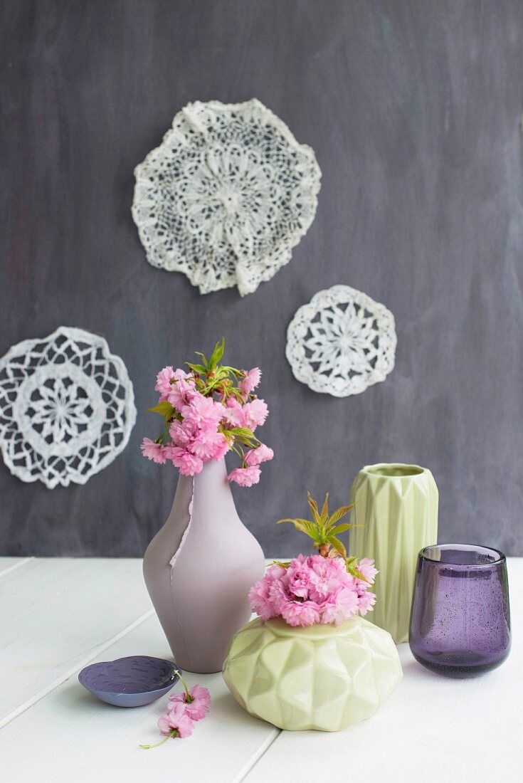 Flowering branches in vases with structured surfaces and lace doilies on wall
