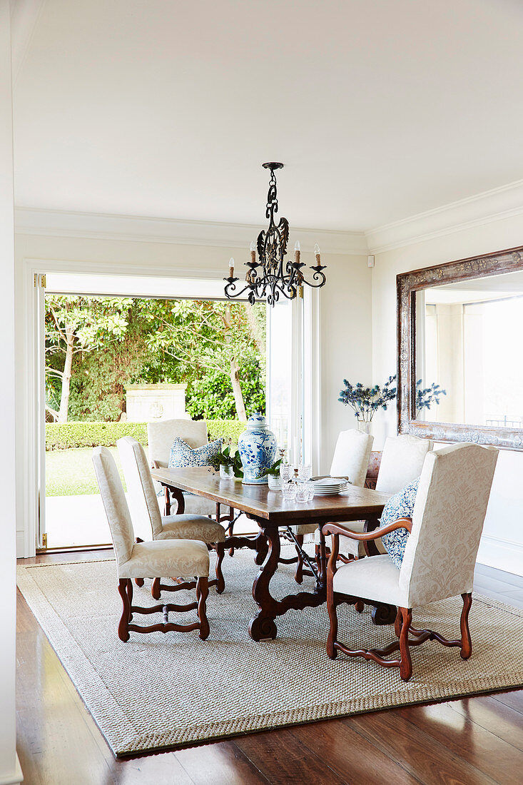 Antique French dining table with upholstered chairs on sisal carpet in front of a patio door