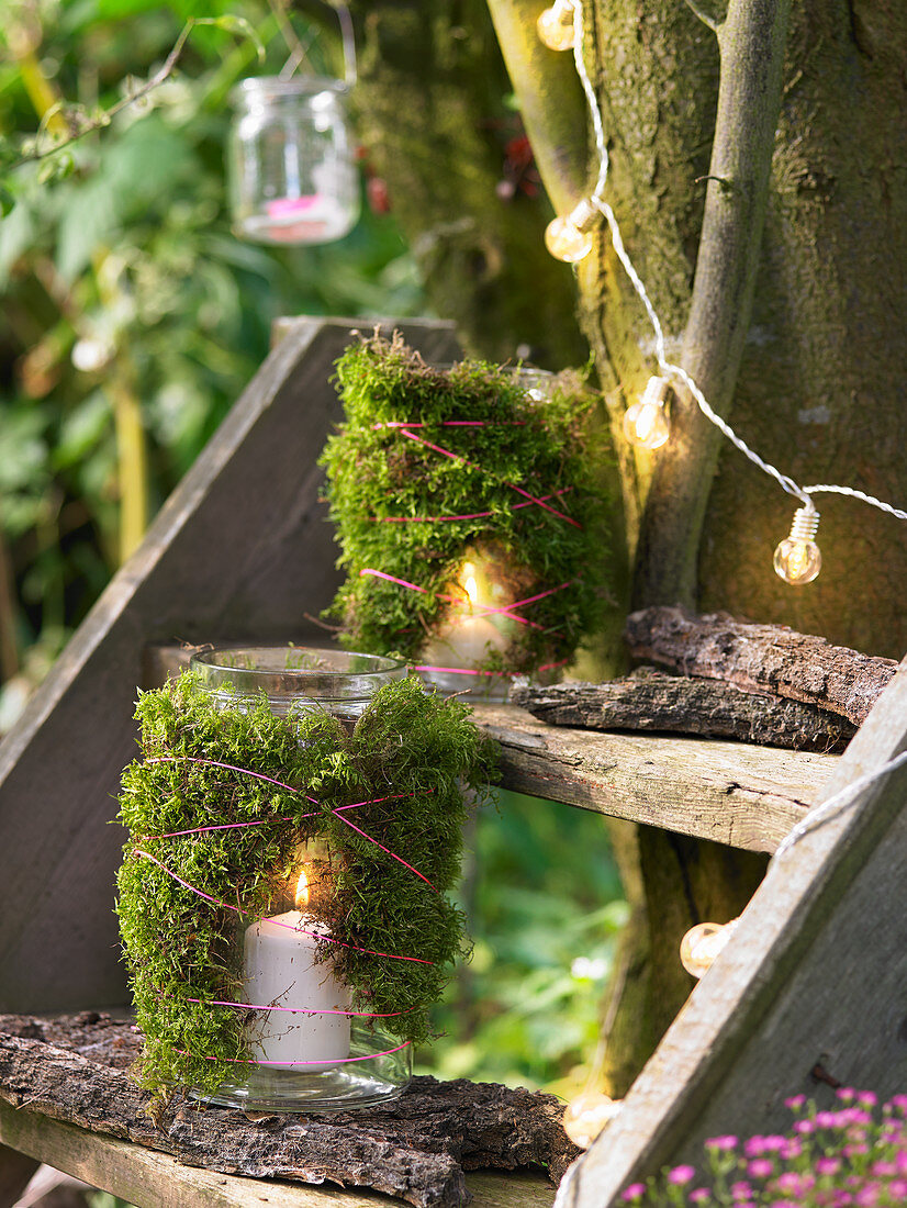 Candle lanterns wrapped in moss on steps next to tree