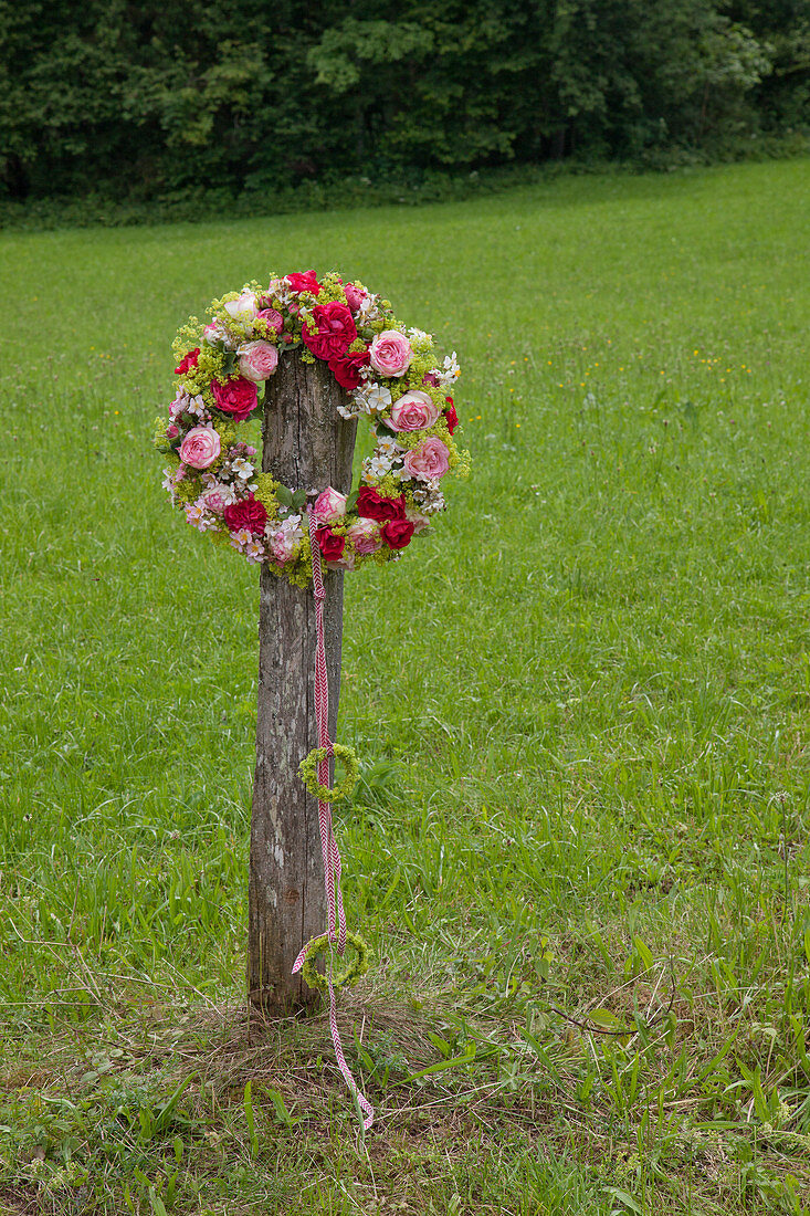 Wreath of roses and lady's mantle hung from wooden post in garden