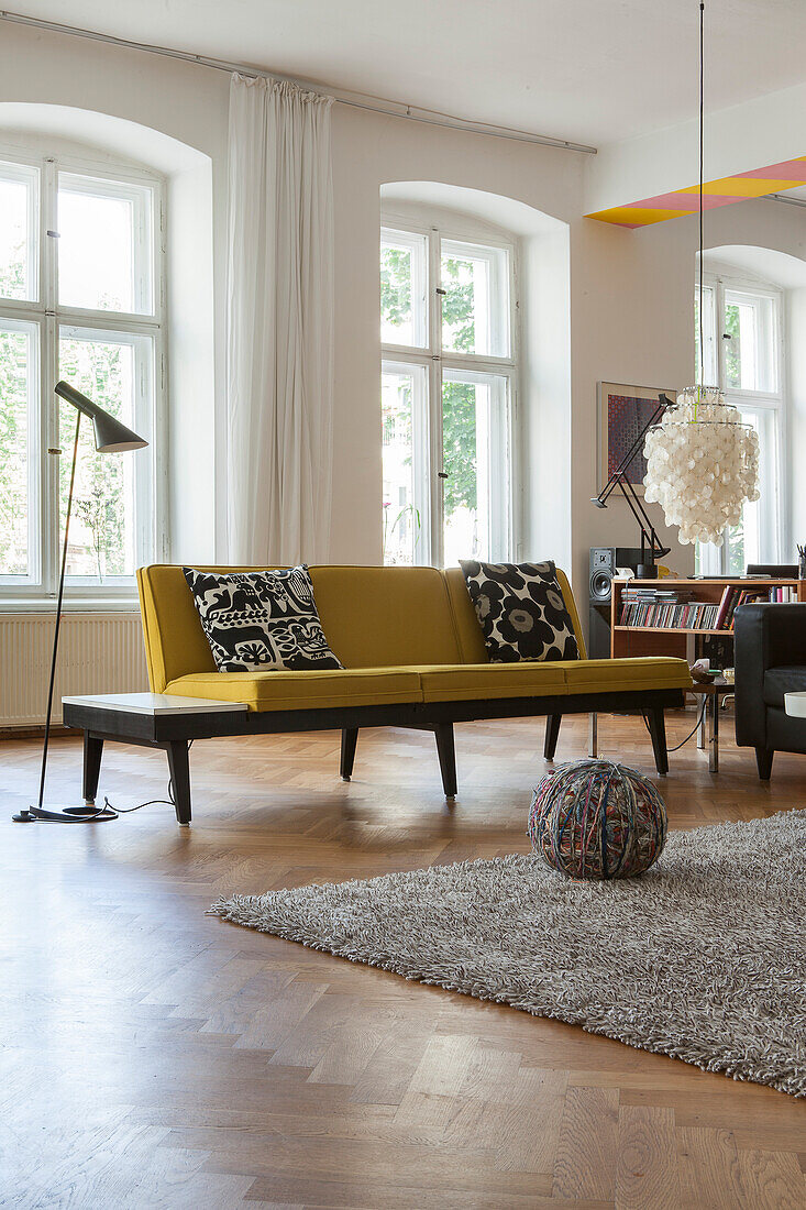 Gelbes Sofa und Stehlampe vor Fenster in Altbauwohnung