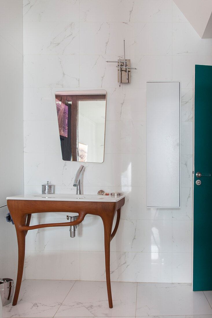 Designer washstand below mirror mounted on marble wall tiles