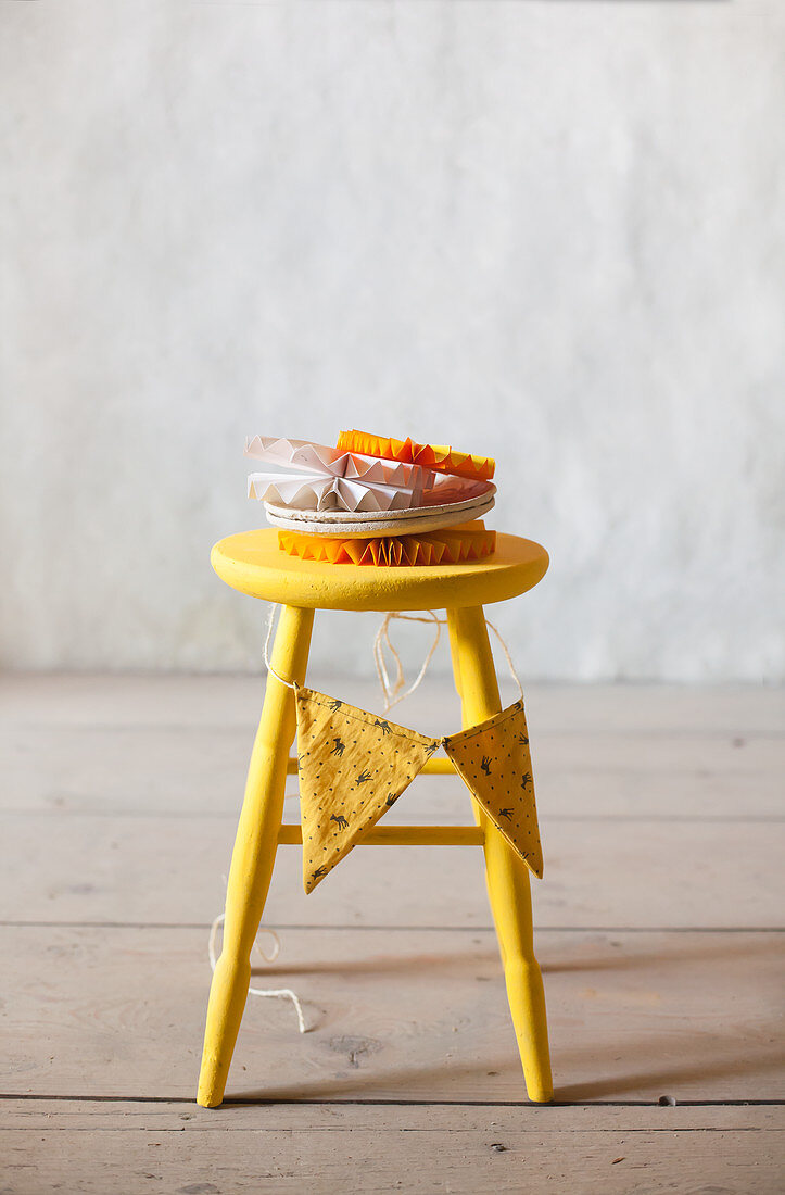 Stack of plates and paper rosettes on yellow stool