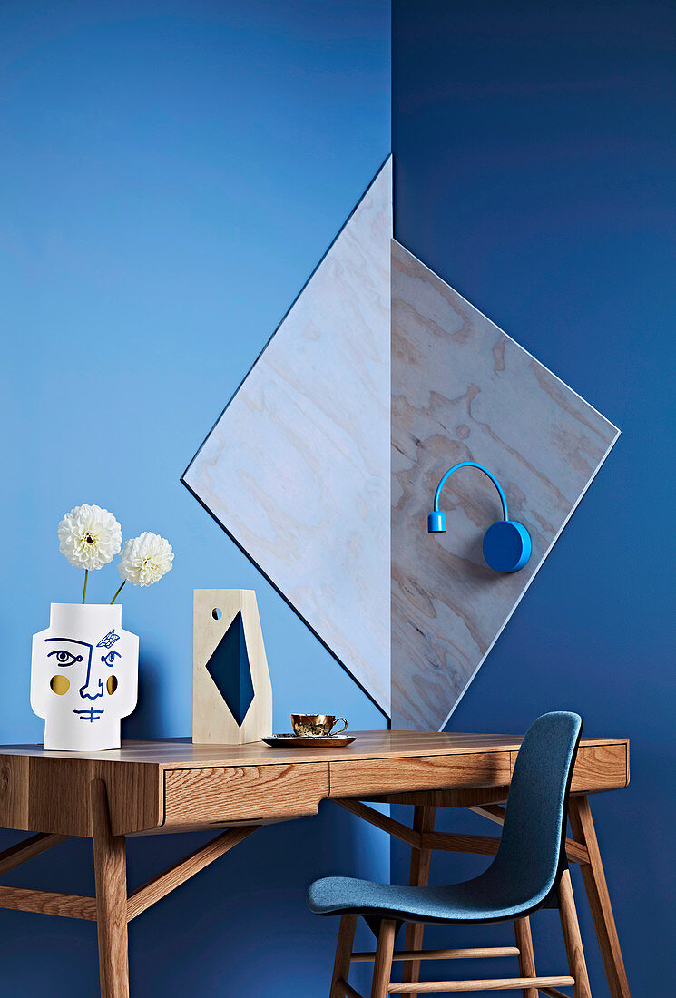 Schreibtisch und Stuhl vor blauer Wand mit geometrischer Dekoration