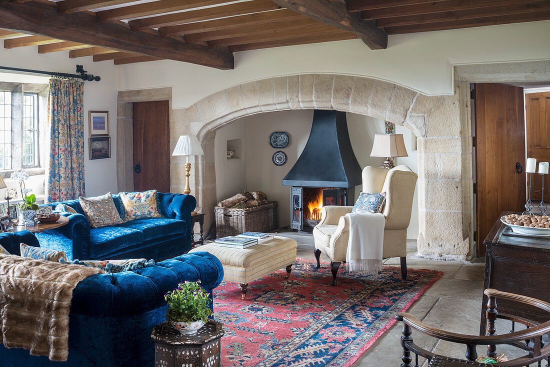 Log burner in inglenook fireplace and blue sofa set in living room of old building