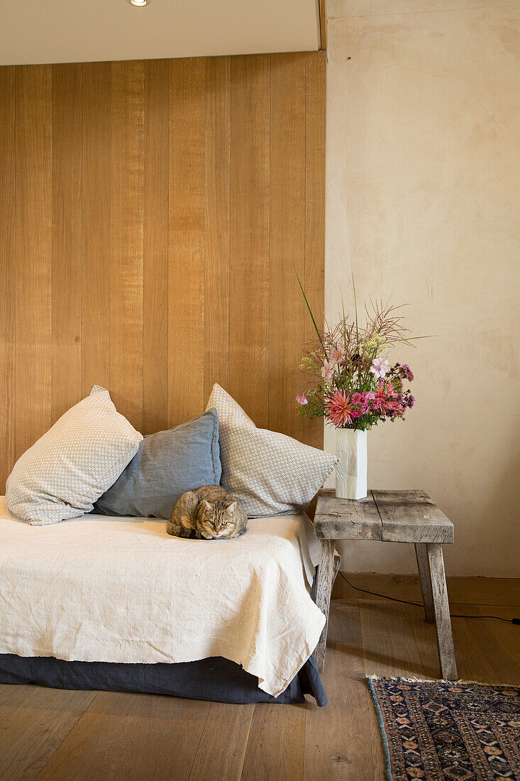 Katze liegt auf Tagesbett, pinker Blumenstrauß auf rustikalem Hocker