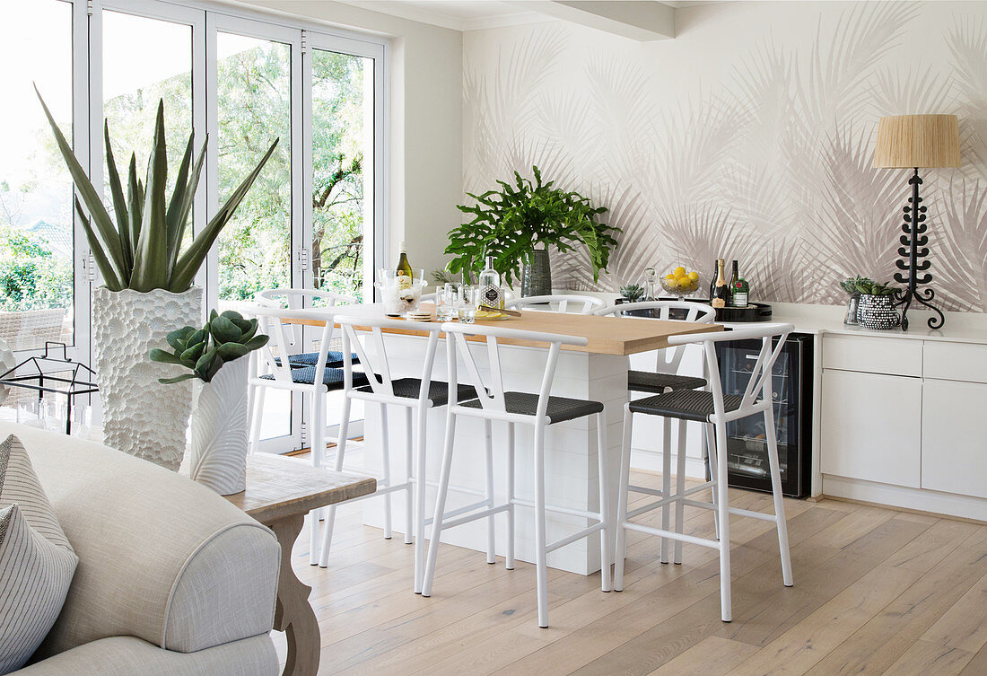 Delicate barstools at kitchen counter in open-plan interior with palm-tree-patterned wallpaper
