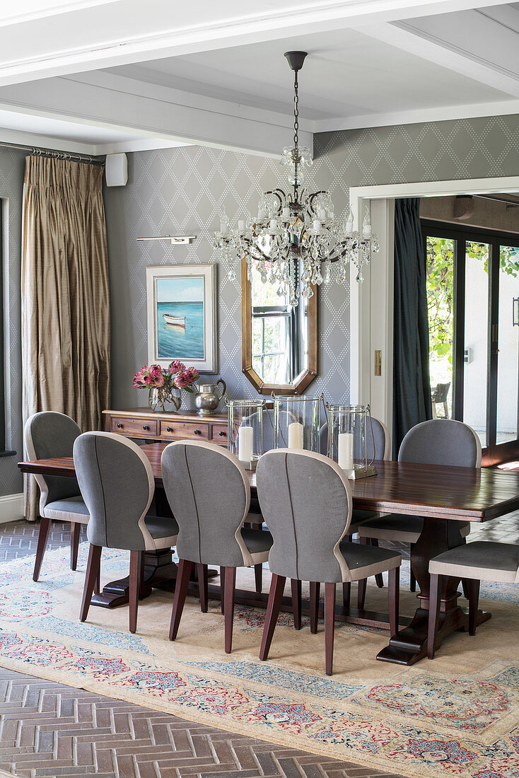 Table, elegant chairs, chandelier and patterned wallpaper in dining room