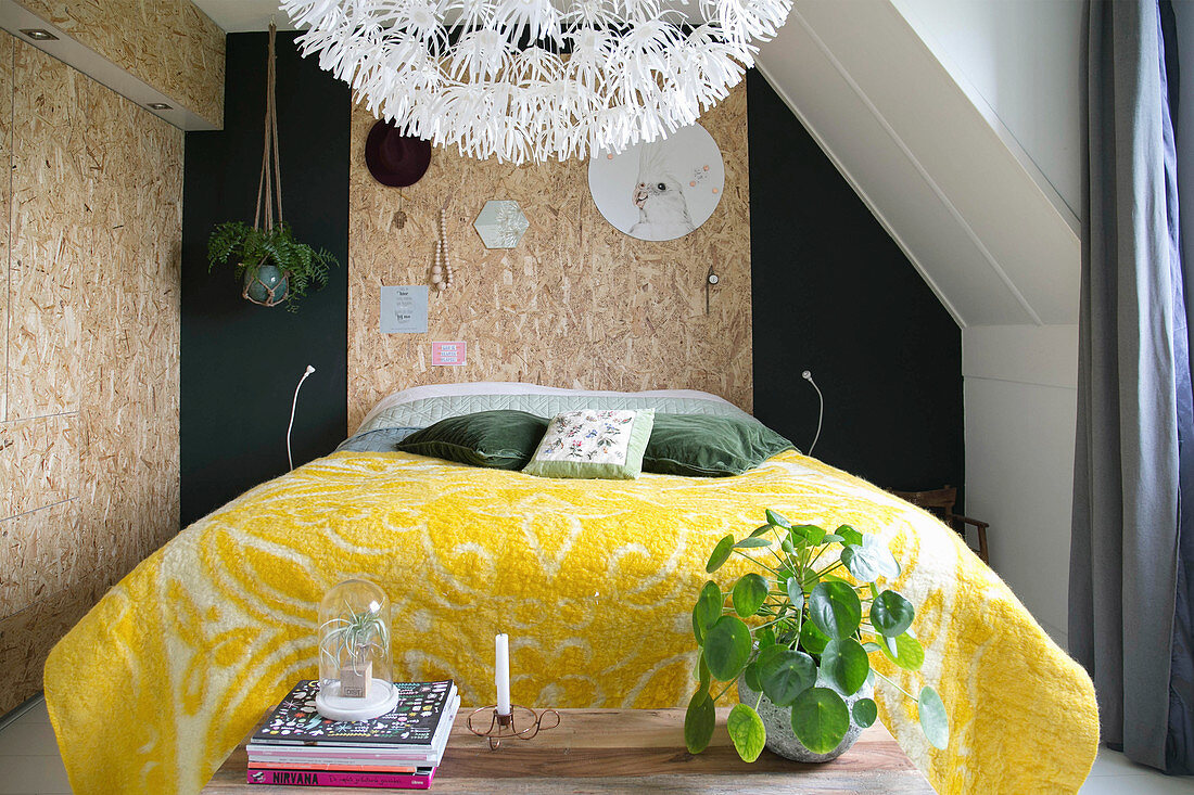 Gelbe Filzdecke auf dem Bett vor einer Wand mit Grobspanplatte