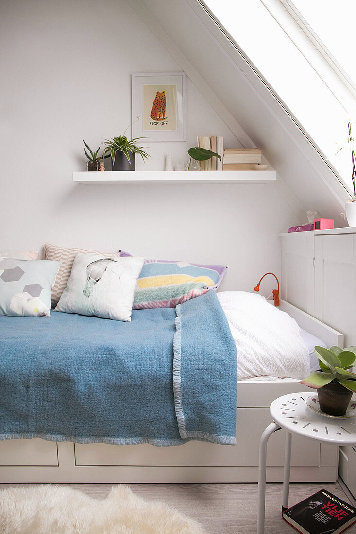Blue blanket on bed with drawers below under sloping ceiling