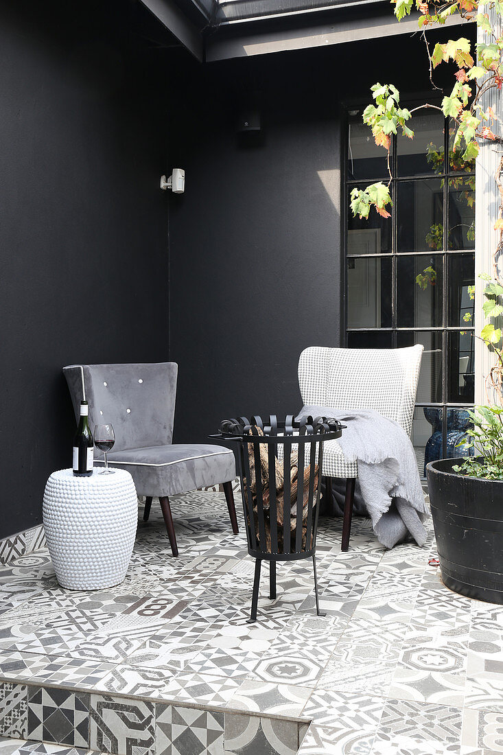 Armchairs and brazier on terrace with dark walls and ornate floor tiles