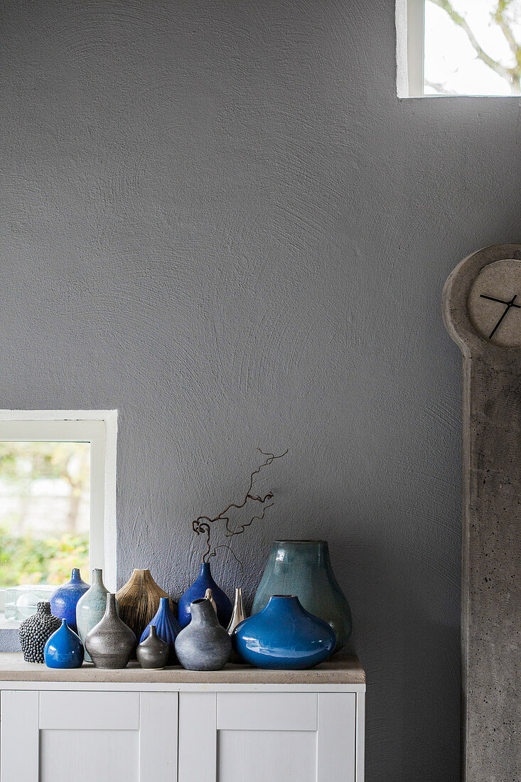 Sammlung von Vasen in Blau und Grau vor grauer Wand