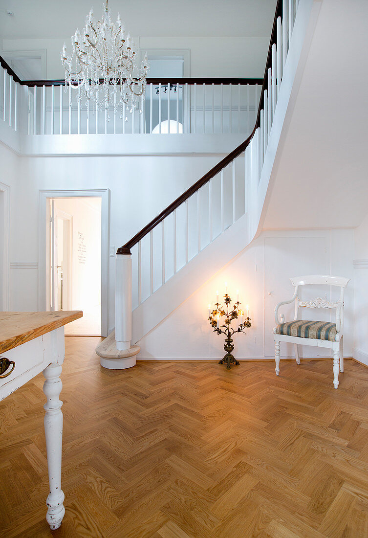 Chair and candelabra in hall with herringbone parquet floor, staircase and white walls