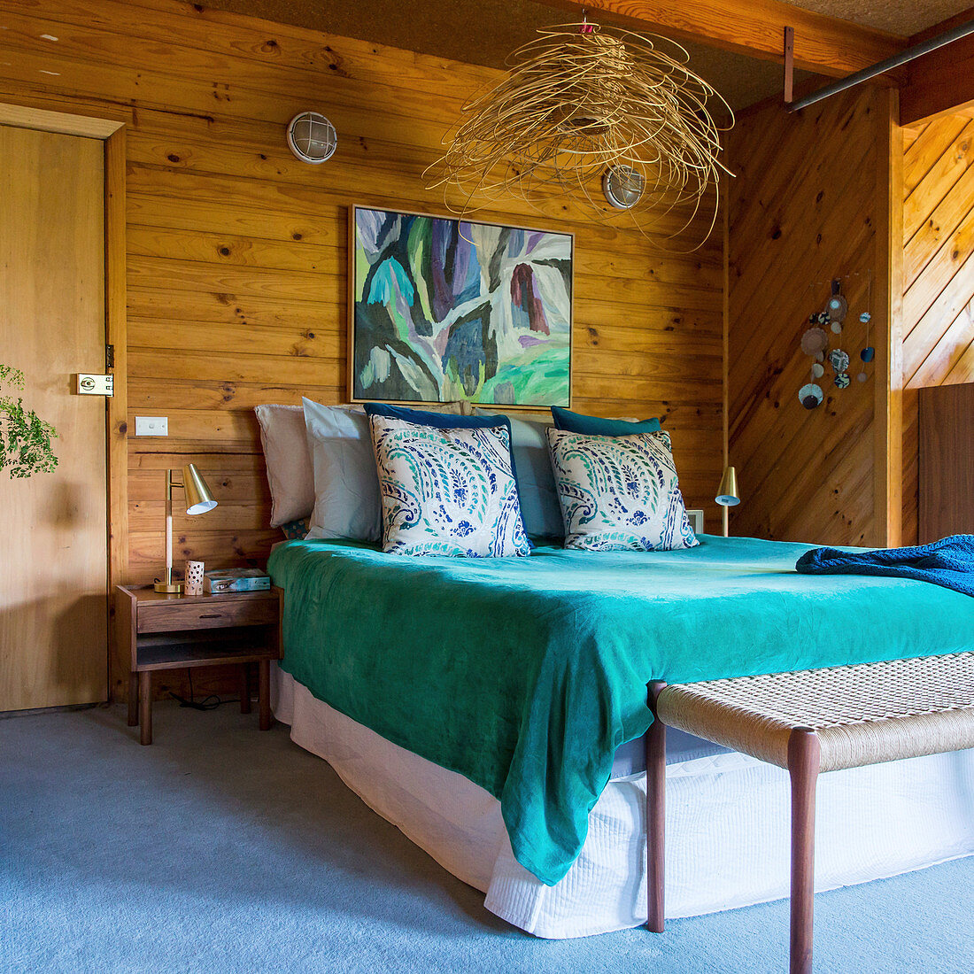 Doppelbett mit türkisfarbener Tagesdecke im Schlafzimmer mit Holzverkleidung