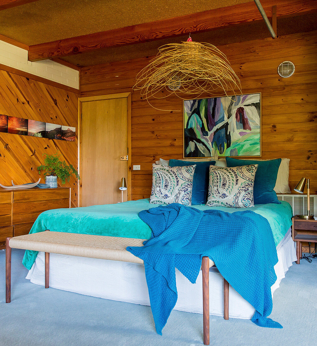 Doppelbett mit türkisfarbener Tagesdecke im Schlafzimmer mit Holzverkleidung