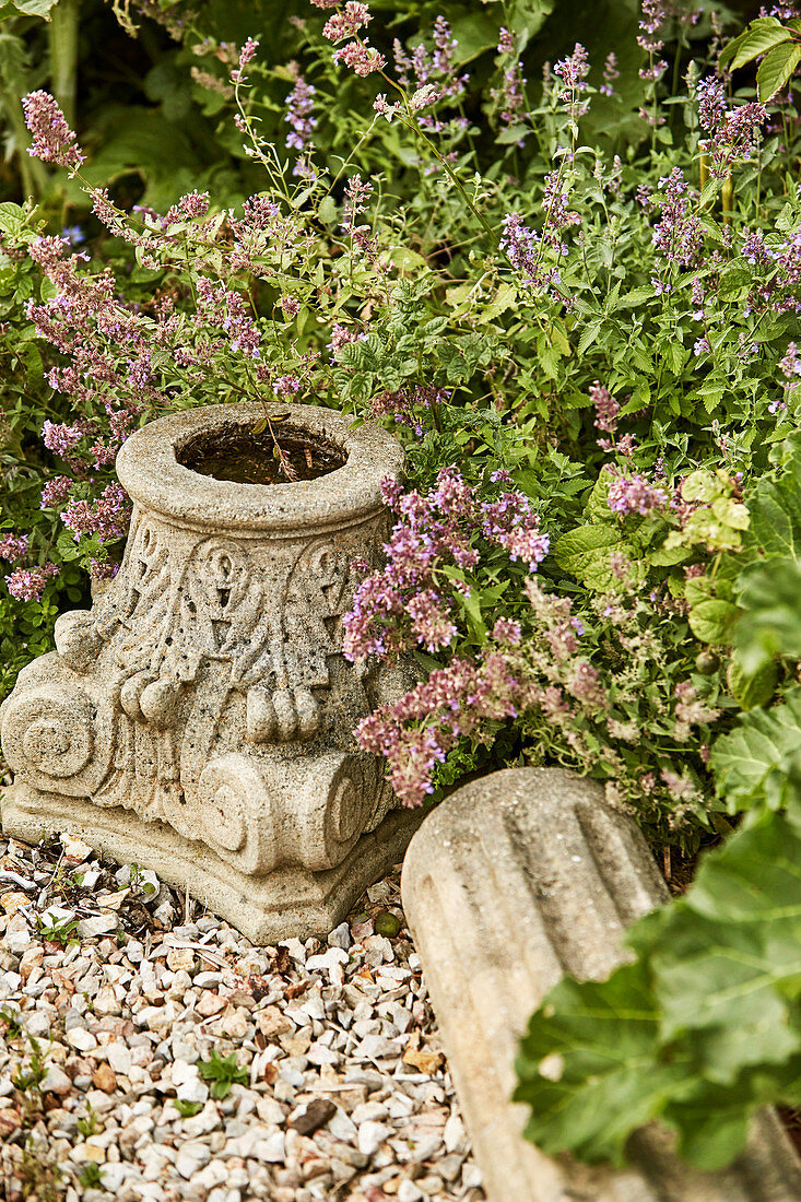 Capital and stone pillar between gravel and plants