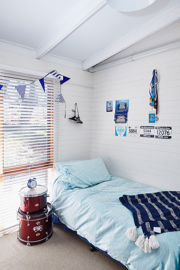 Trommeln als Nachttisch neben Bett im Jungenzimmer mit weiß gestrichener Holzverkleidung