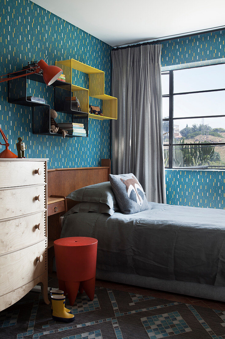 Shelving modules above bed in child's bedroom with blue-patterned wallpaper