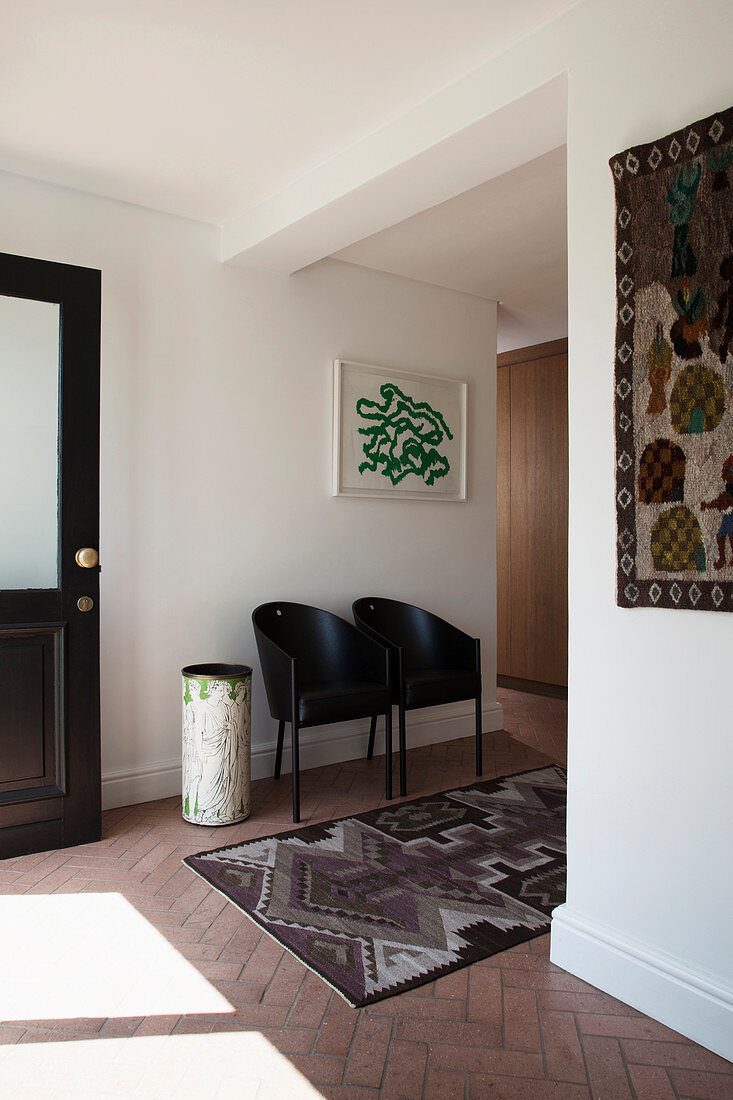 Two black designer chairs and ethnic rug in foyer