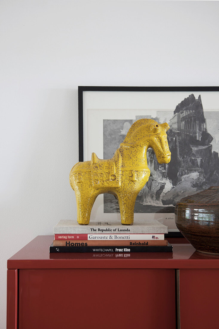Gelbe Pferdeskulptur auf einem Bücherstapel auf rotem Schrank