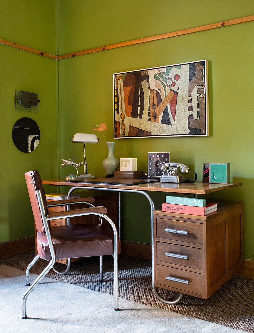 Alter Schreibtisch aus Holz mit Metallgestell vor grüner Wand