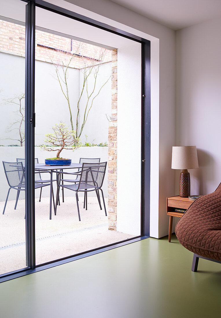 Blick durch die offene Terrassentür auf Tisch und Stühle mit Bonsai