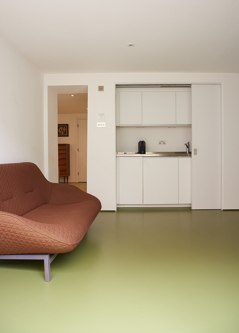 Braunes Sofa auf grünem Boden vor Küchenzeile mit Schiebetür
