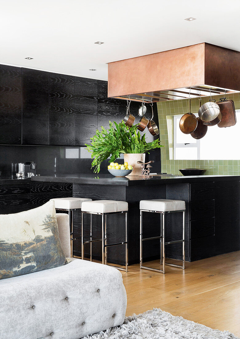 Dark fitted kitchen with counter and barstools in open-plan interior