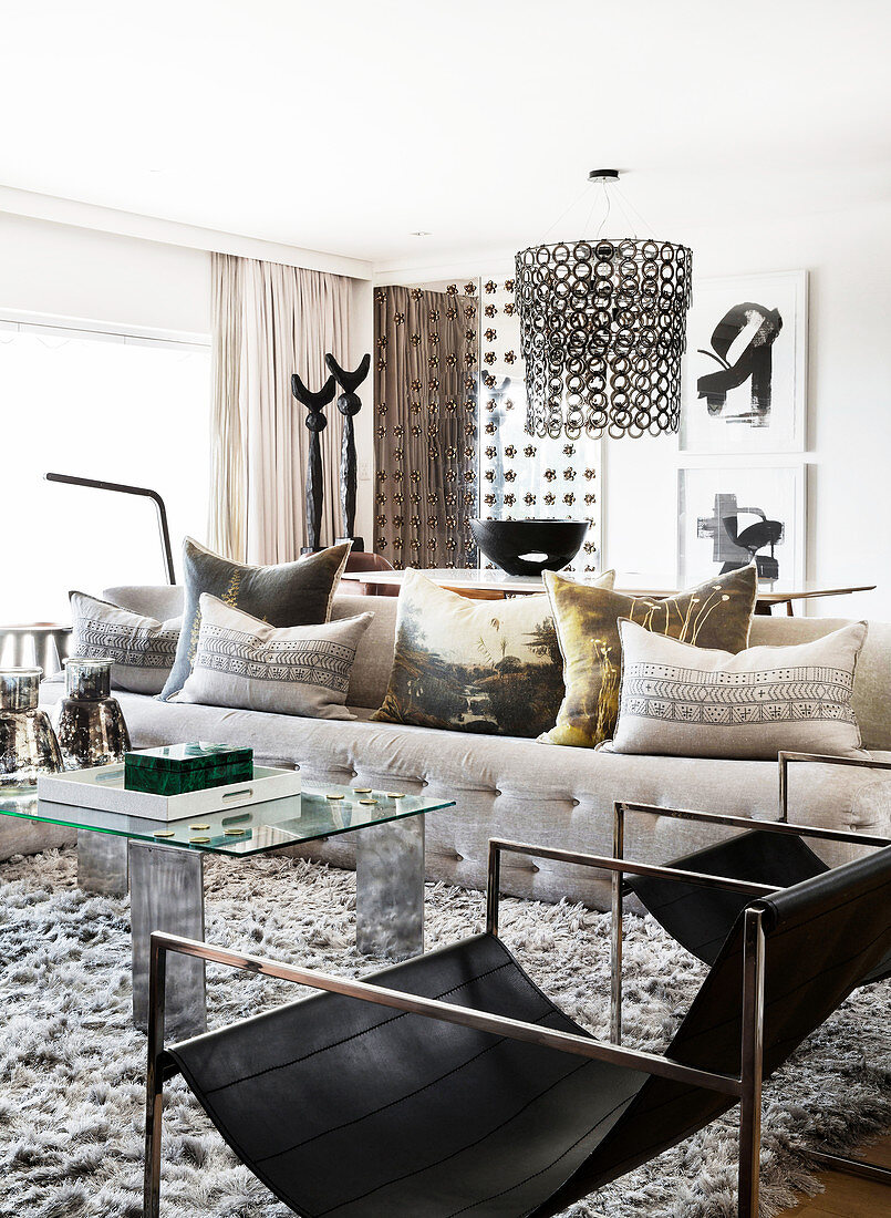 Sofa mit Kissen, Couchtisch aus Glas und Designerstuhl in hellem Wohnzimmer