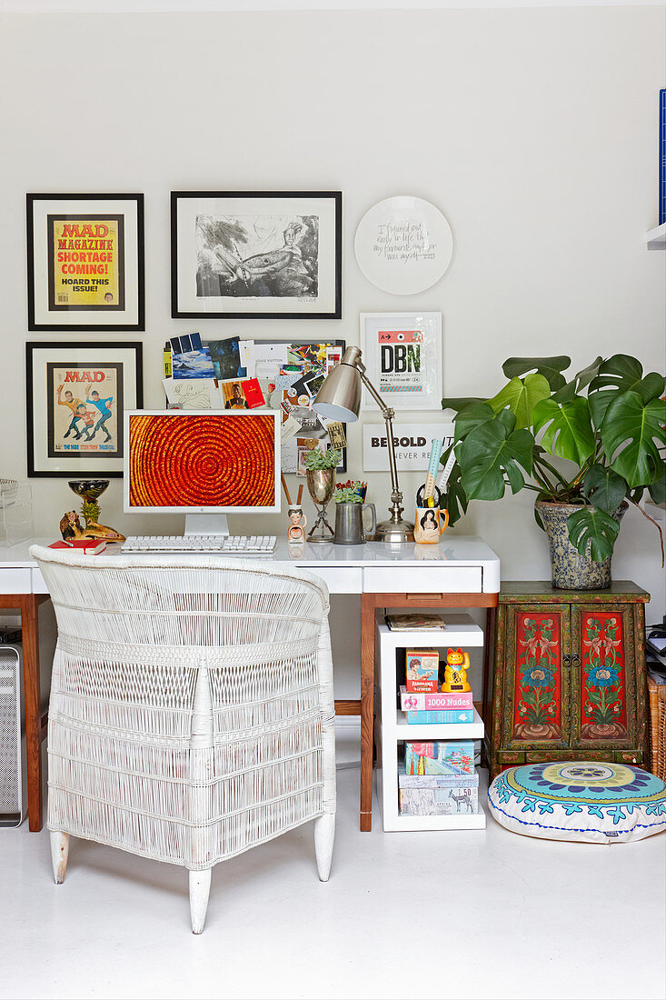 Korbstuhl am Schreibtisch mit Bilderwand und exotischer Deko