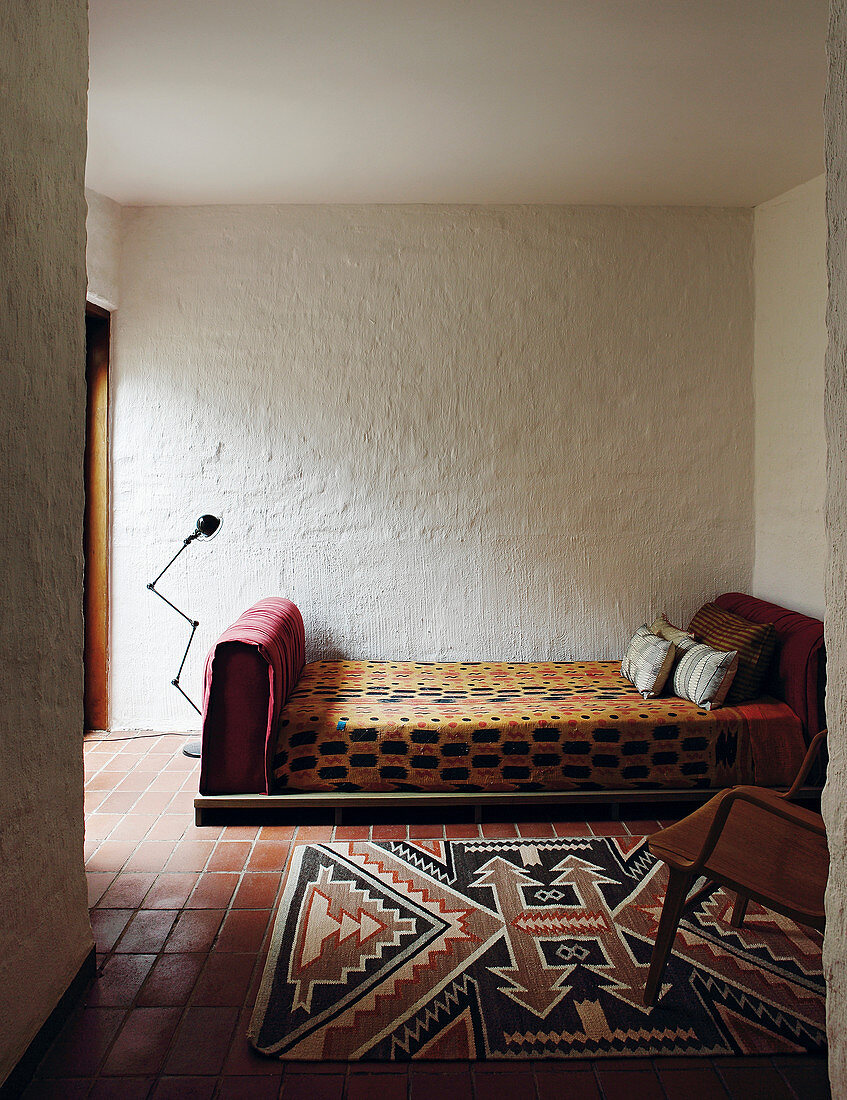 Tagesbett und Teppich im Ethnostil vor grob verputzten Wänden