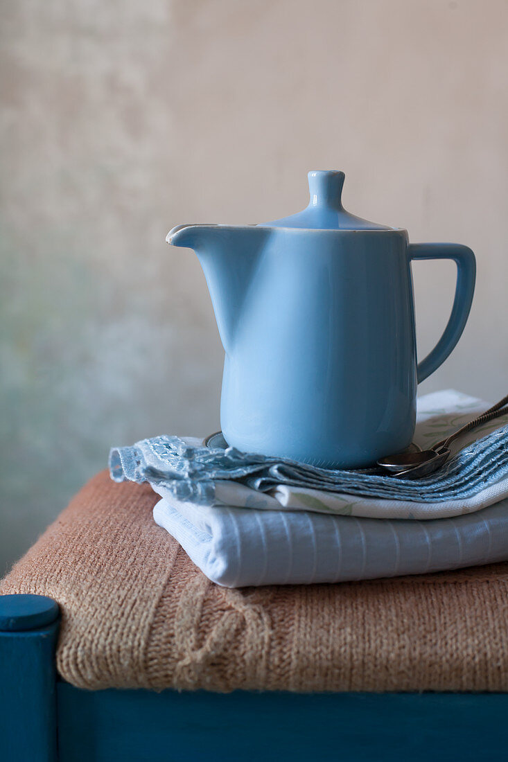 Blue coffee pot and stacked cloths on stool