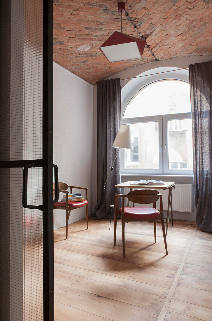 Tisch, Stühle und Stehlampe im Zimmer mit Rundbogenfenster und Ziegeldecke