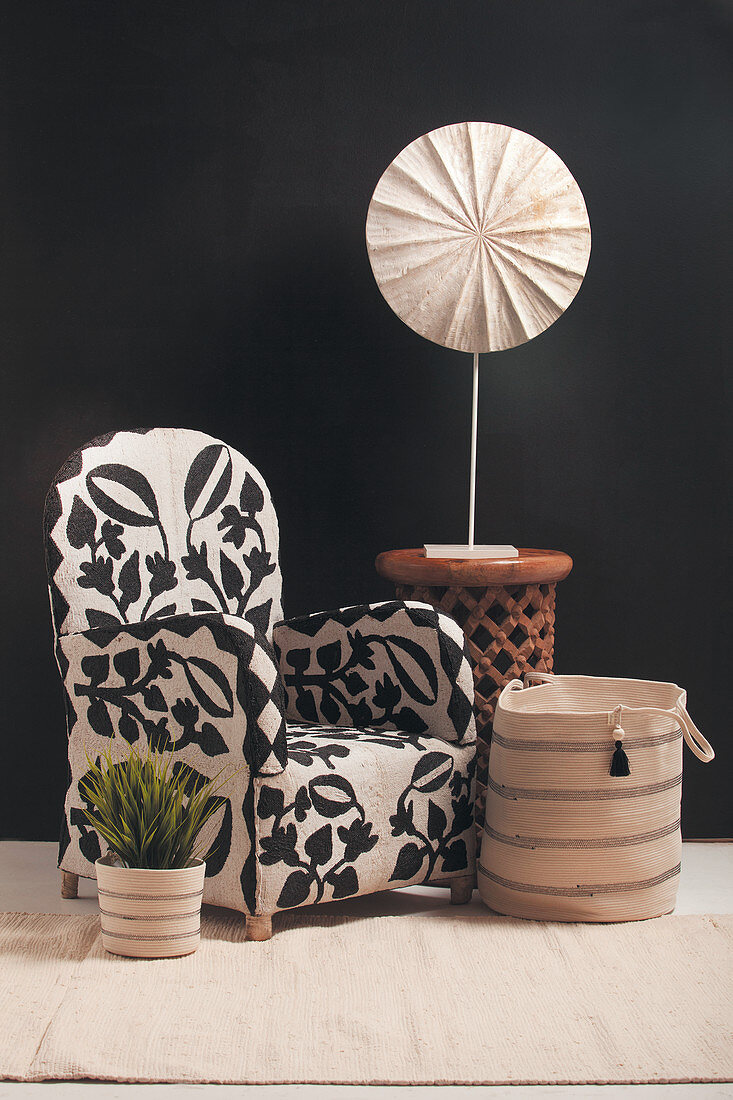 Patterned armchair, fabric basket and side table in front of black wall