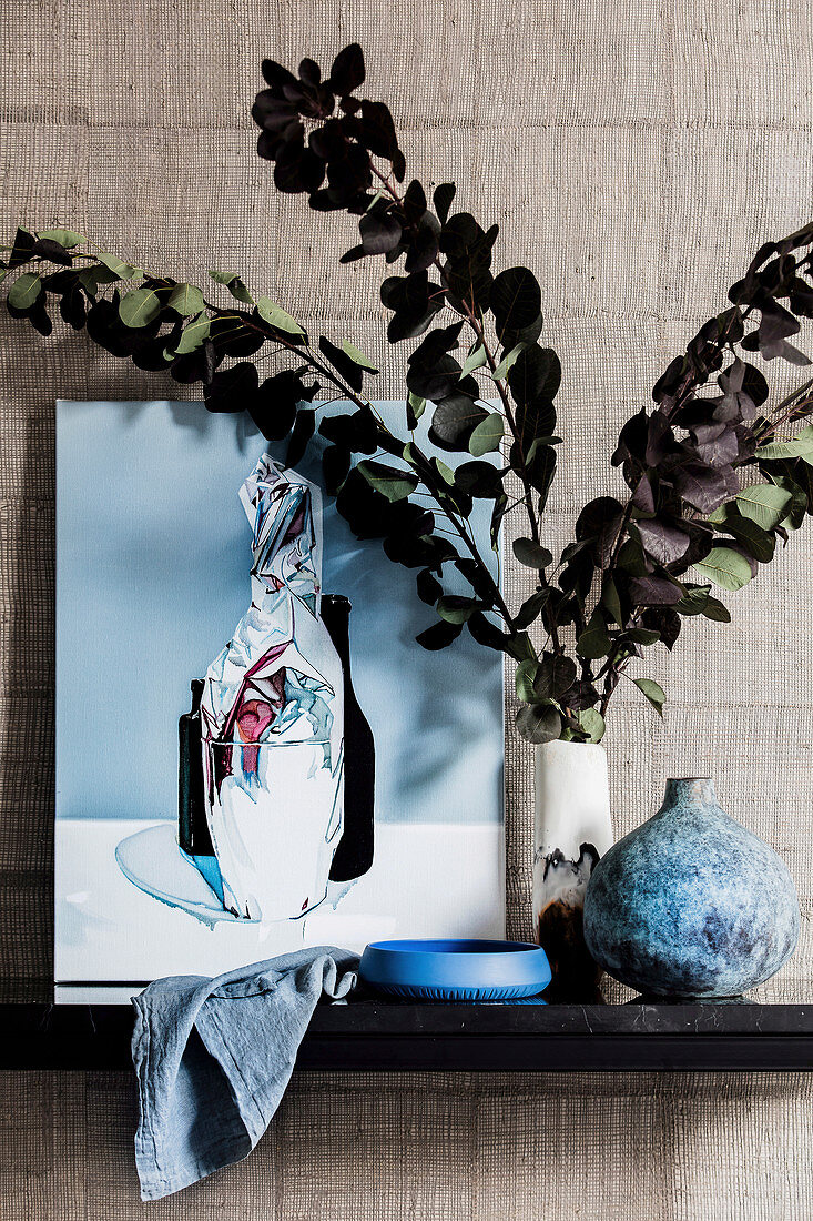 Bild und Vase mit Blätterzweigen vor Wand mit Designertapete