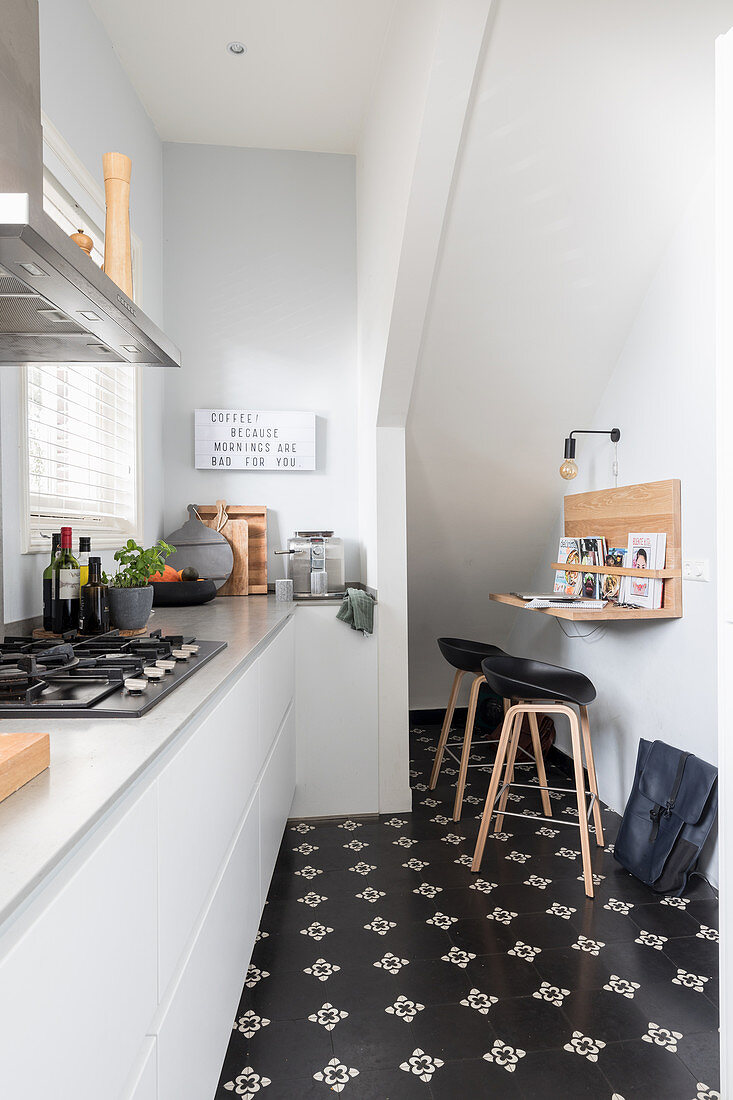 weiße Einbauküche und kleine Frühstückstheke mit Barhockern unter Treppenwand